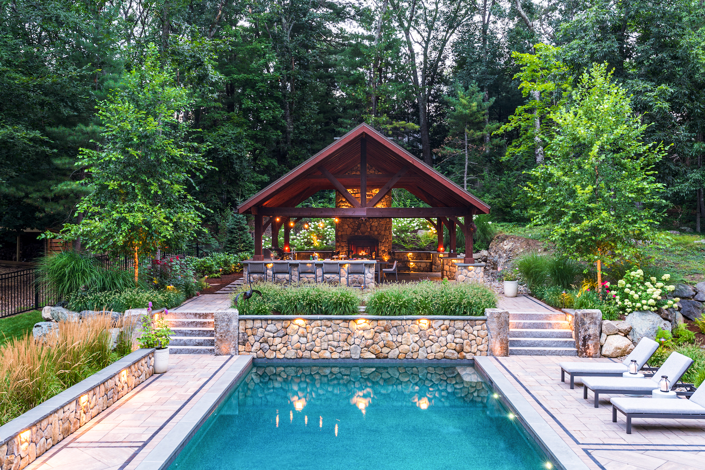 Pool lined with luscious landscape and a stone fireplace