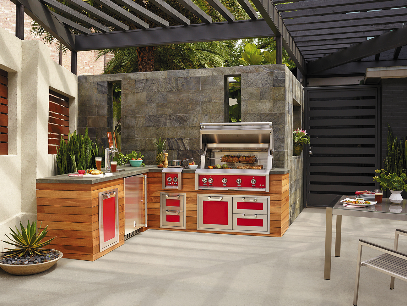 Backyard Patio kitchen with red appliances and a stone countertop with food being prepared and meat being grilled