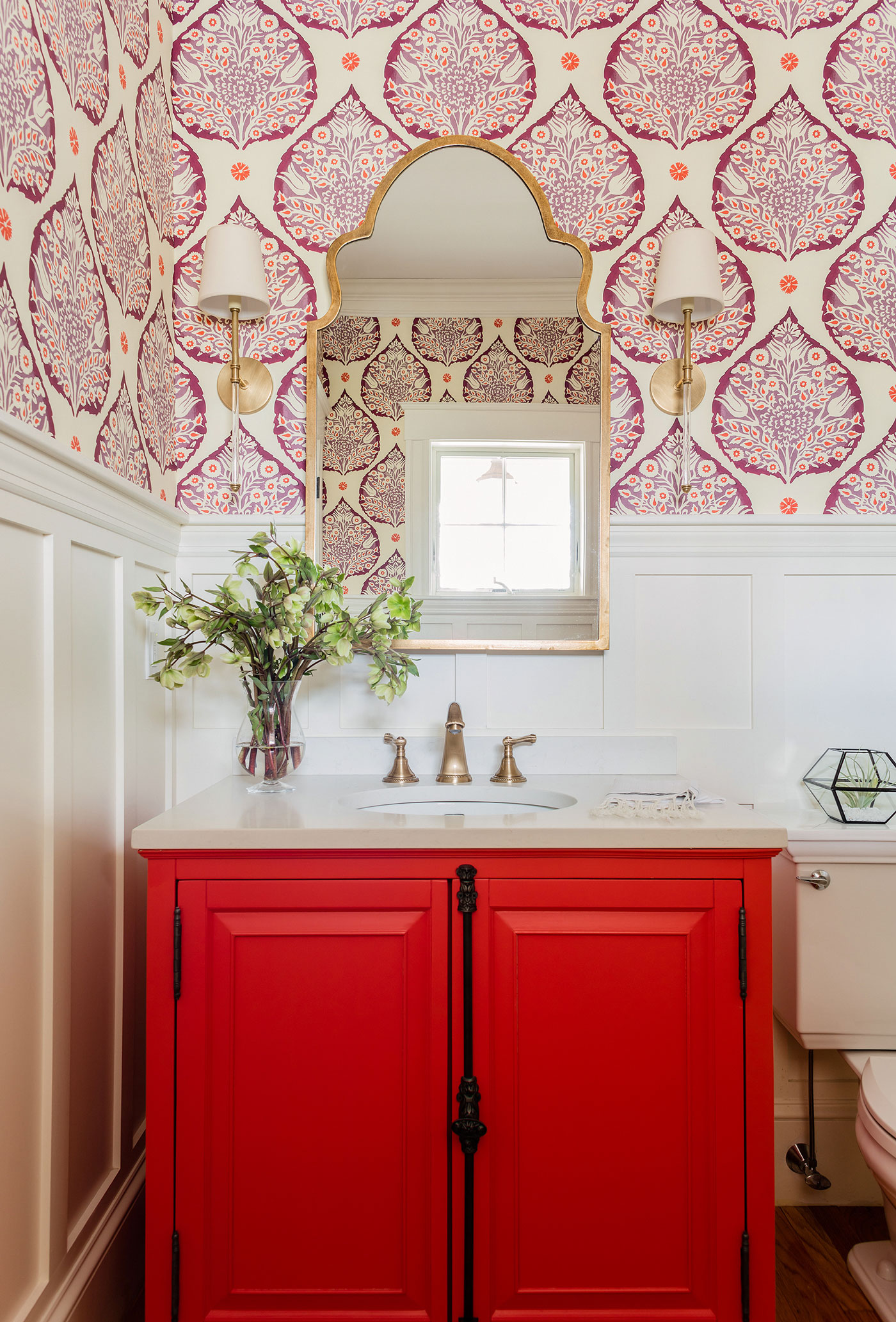 Colorful powder room with red cabinet doors and white paneled walls